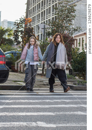 Cute mother and daughter hold each other's hand and cross the road at a crosswalk 126629879