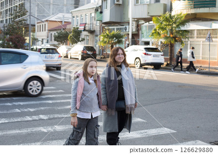 Pretty mother and daughter hold each other's hand and cross the road at a crosswalk Pretty mother and daughter hold each other's hand and cross the road at a crosswalk 126629880