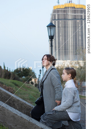 Outdoors portrait of woman and young girl child walking along the streets of the city. Outdoors portrait of woman and young girl child walking along the streets of the city. 126629905