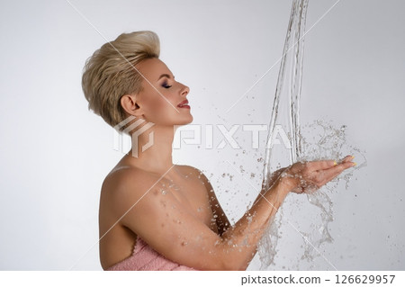 Elegant woman enjoying water splashes against a clean backdrop in soft lighting 126629957