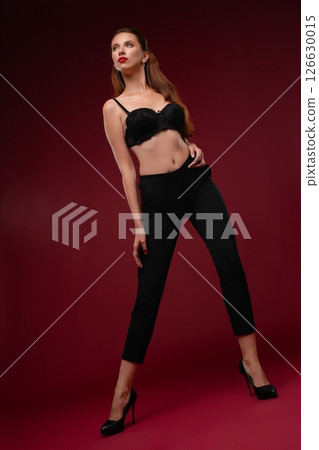 Stylish woman posing in lingerie against a rich red background in a studio 126630015