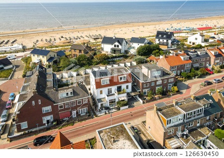 The image showcases a picturesque aerial view of a beach town, featuring residential houses, sandy beaches, and a vibrant coastal atmosphere. 126630450