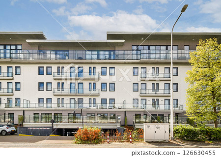 A contemporary multi-story apartment building featuring balconies, large windows, and a landscaped entrance, set against a bright blue sky. A contemporary multi-story apartment building featuring balconies, large windows, and a landscaped entrance, set against a bright blue sky. 126630455