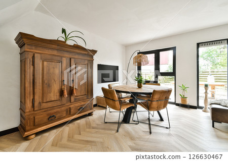 Stylish living room featuring a wooden cabinet, elegant furniture, and natural light streaming through large windows, creating a warm and inviting atmosphere. 126630467