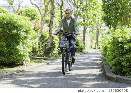 A middle-aged man riding an electric bike among the fresh greenery A middle-aged man riding an electric bike among the fresh greenery 126630498