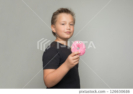 Handsome child boy holding testy donut. Kid in black t-shirt with sweet food indoor 126630686