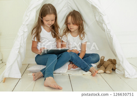 Beautiful little girl sisters with tablet pc computer in kids tent at home.  126630751