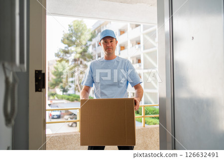A male courier in a blue uniform with a parcel in his hands. 126632491