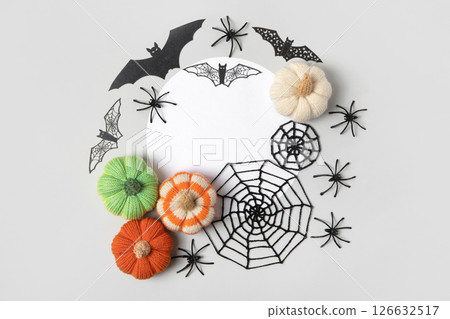 Halloween composition of knitted orange and green pumpkins, black cobwebs and spiders and bats with a round white place for text. Handmade knitted toys for children and holiday home decor. Halloween composition of knitted orange and green pumpkins, black cobwebs and spiders and bats with a round white place for text. Handmade knitted toys for children and holiday home decor. 126632517