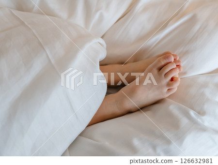 The feet of a small child in a parent's bed on white sheets rolled in a white blanket . High quality photo The feet of a small child in a parent's bed on white sheets rolled in a white blanket . High quality photo 126632981