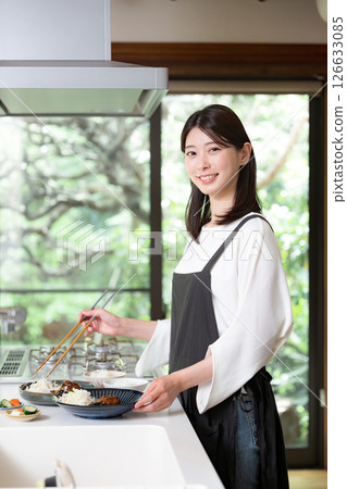 A woman wearing an apron preparing a meal, looking at the camera 126633085