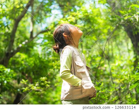 A happy little girl is exploring the forest and looking at the leaves. Adventure tourism and learning concept. A happy little girl is exploring the forest and looking at the leaves. Adventure tourism and learning concept. 126633114