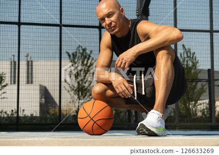 Basketball player sits and relax after workout at sport stadium. Professional athlete or sportsman with accident. Outdoor. Sport leisure activity. Basketball player sits and relax after workout at sport stadium. Professional athlete or sportsman with accident. Outdoor. Sport leisure activity. 126633269