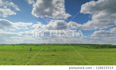 A Serene Green Landscape Featuring Fluffy White Clouds in a Bright Blue Sky Setting Time lapse. 126633514