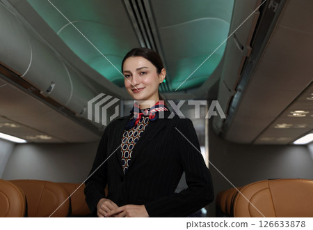 Flight attendant or Air Hostess. A friendly flight attendant stand confidently inside an airplane cabin. Professional hospitality and elegant uniform. Aviation service travel airline Flight attendant. Flight attendant or Air Hostess. A friendly flight attendant stand confidently inside an airplane cabin. Professional hospitality and elegant uniform. Aviation service travel airline Flight attendant. 126633878