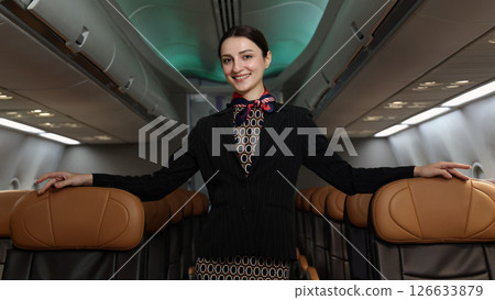 Flight attendant or Air Hostess. A friendly flight attendant stand confidently inside an airplane cabin. Professional hospitality and elegant uniform. Aviation service travel airline Flight attendant. 126633879