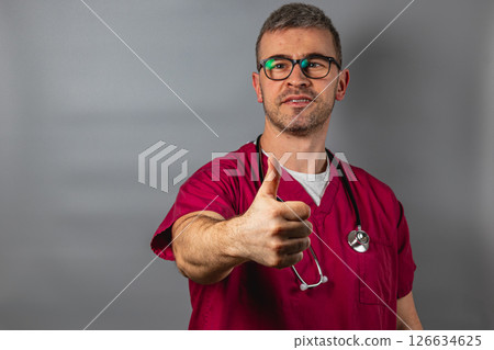 Doctor in scrubs giving a thumbs up against a gray backdrop Doctor in scrubs giving a thumbs up against a gray backdrop 126634625