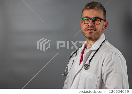 Doctor in white coat smiling indoors with stethoscope and glasses 126634629