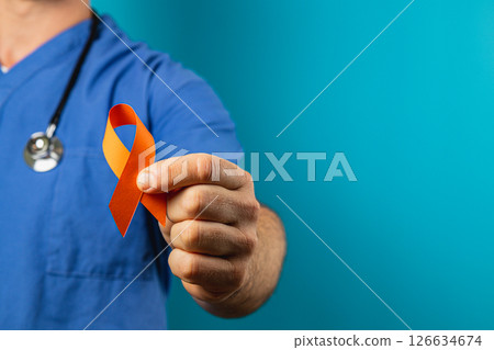 Medical professional holding orange awareness ribbon against blue background Medical professional holding orange awareness ribbon against blue background 126634674