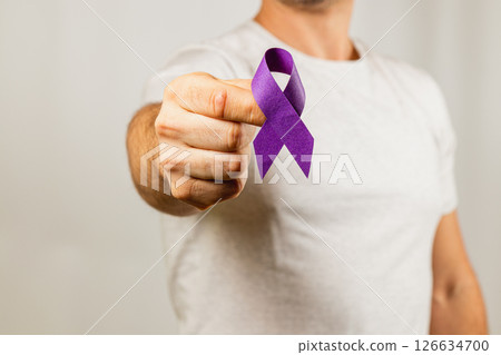 Man holds purple ribbon for awareness against a neutral background Man holds purple ribbon for awareness against a neutral background 126634700