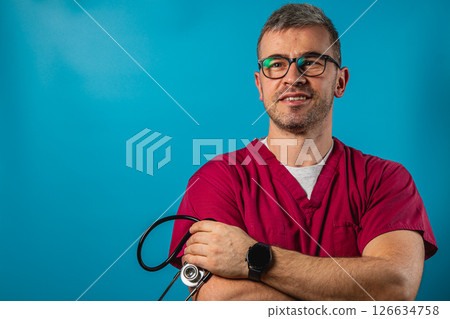 Healthcare professional in scrubs with stethoscope against blue background Healthcare professional in scrubs with stethoscope against blue background 126634758