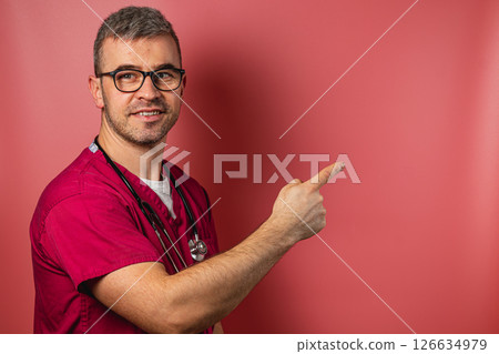 Medical professional in scrubs pointing to a blank wall background Medical professional in scrubs pointing to a blank wall background 126634979