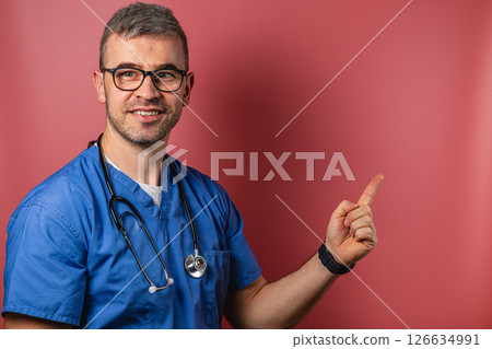 Doctor in scrubs gestures towards a blank space with a friendly smile 126634991
