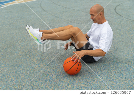 Basketball player or sporty man sitting, have fun with ball on sports court at courtyard. Urban style. Copy space. 126635967