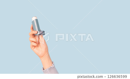 Woman holding asthma inhaler isolated light blue background. Pharmaceutical products is used to prevent and treat wheezing and shortness of breath caused asthma or COPD. Woman holding asthma inhaler isolated light blue background. Pharmaceutical products is used to prevent and treat wheezing and shortness of breath caused asthma or COPD. 126636599