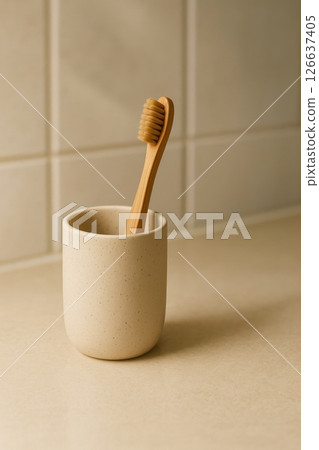 Bamboo toothbrush in ceramic cup on beige bathroom countertop with tiled wall background, natural eco bathroom accessory 126637405
