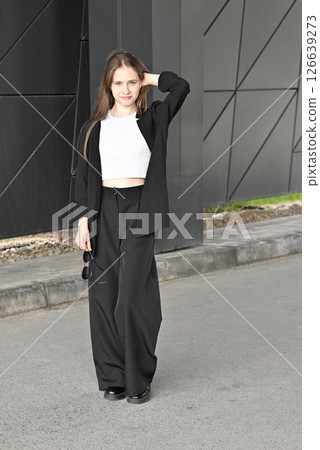 Woman walking in stylish outfit holding sunglasses near modern geometric wall. 126639273