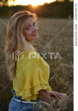 Woman stands in a golden field of wheat during sunset, showcasing natural beauty and serenity in a rural setting Woman stands in a golden field of wheat during sunset, showcasing natural beauty and serenity in a rural setting 126639276