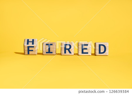 Flipping wooden cube blocks with FIRED to HIRED text over yellow background 126639384