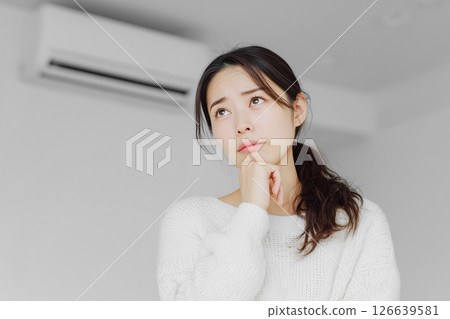 The expression of a young woman who is worried about whether to repair or replace her broken air conditioner 126639581