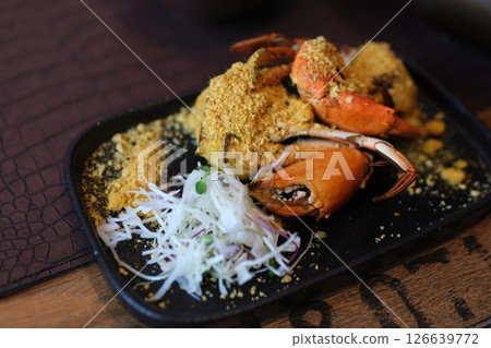 Close-up of hands setting a colorful crab stir fry on a table, showcasing its rich texture and garnishes. 126639772