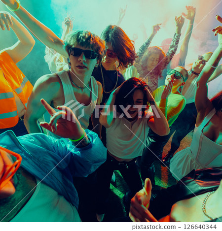 Crowd of young people dancing energetically under colorful lights at a party or concert. 126640344