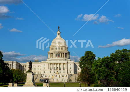 U.S. Capitol Building shines under blue sky, fluffy clouds, lush green trees. 126640459