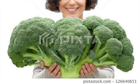 In a joyful moment, an adult woman holds up an impressive bunch of broccoli, expressing pride and enthusiasm for healthy eating. Her smile adds to the vibrant atmosphere. 126640651