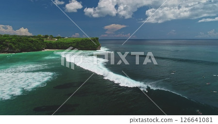 Stunning aerial drone footage capturing surfers riding perfect waves at the famous Dreamland Beach in Bali, Indonesia, showcasing the vibrant turquoise waters and lush green cliffs 126641081