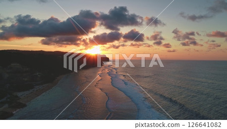 Golden sunset illuminating breaking ocean waves on a beautiful beach on the coast of Bali, Indonesia, with cliffs and colorful clouds creating a breathtaking view Golden sunset illuminating breaking ocean waves on a beautiful beach on the coast of Bali, Indonesia, with cliffs and colorful clouds creating a breathtaking view 126641082