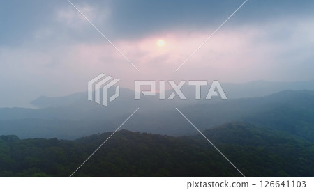 Layers of misty mountains and forest fading into the distance as the sun sets behind a cloudy sky, creating a serene and atmospheric landscape Layers of misty mountains and forest fading into the distance as the sun sets behind a cloudy sky, creating a serene and atmospheric landscape 126641103