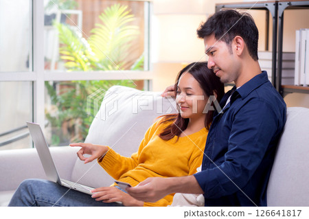 Happy asian couple using laptop and credit card for online shopping together in living room. 126641817