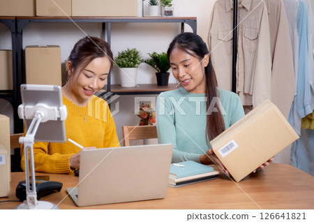 Two young asian woman working while planning online business and checking order with writing. Two young asian woman working while planning online business and checking order with writing. 126641821