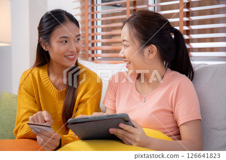 Two young asian woman sitting on sofa using tablet computer shopping online with credit card. Two young asian woman sitting on sofa using tablet computer shopping online with credit card. 126641823