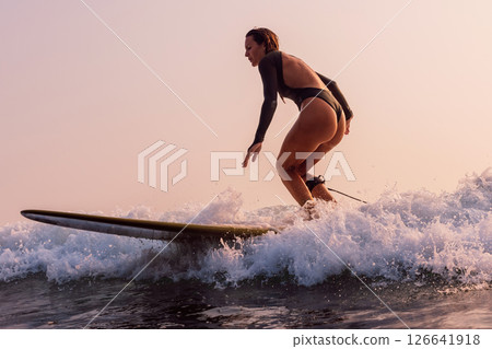 Attractive surf girl in sexy swimsuit rides on surfboard with warm sunlight. Woman riding on longboard. Attractive surf girl in sexy swimsuit rides on surfboard with warm sunlight. Woman riding on longboard. 126641918