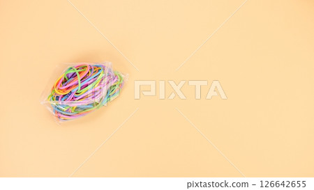 Colorful rubber bands in a clear plastic bag on a solid peach-colored background. Colorful rubber bands in a clear plastic bag on a solid peach-colored background. 126642655