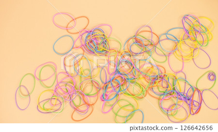 A Tangled Pile of Colorful Rubber Bands Displayed on a Soft Peach Colored Background Surface A Tangled Pile of Colorful Rubber Bands Displayed on a Soft Peach Colored Background Surface 126642656