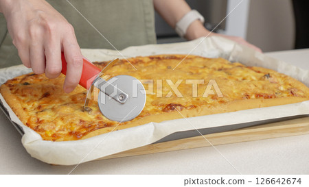 Cutting pizza with a round cutter knife. Close-up of delicious pizza being cut into pieces. Slow motion slicing a pizza into multiple slices with a cutter. 126642674