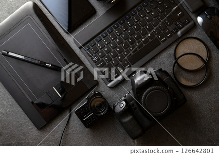 A black camera lies on a table with a pen, a keyboard and more photography and video accessories. A black camera lies on a table with a pen, a keyboard and more photography and video accessories. 126642801