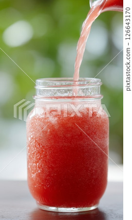 A vibrant jargarita is poured into a mason jar, showcasing the jam mixing with juice, perfect for summer 126643170